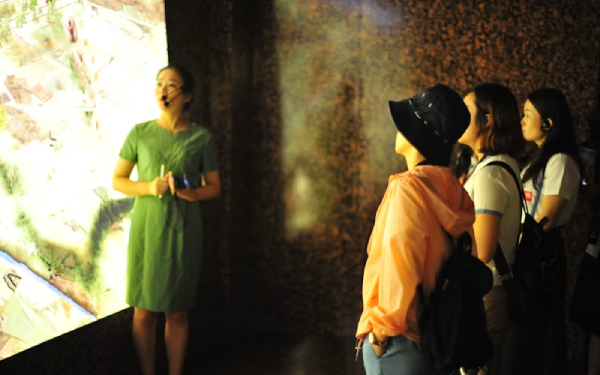 Woman standing in a dim textured hallway with a blurred figure passing by